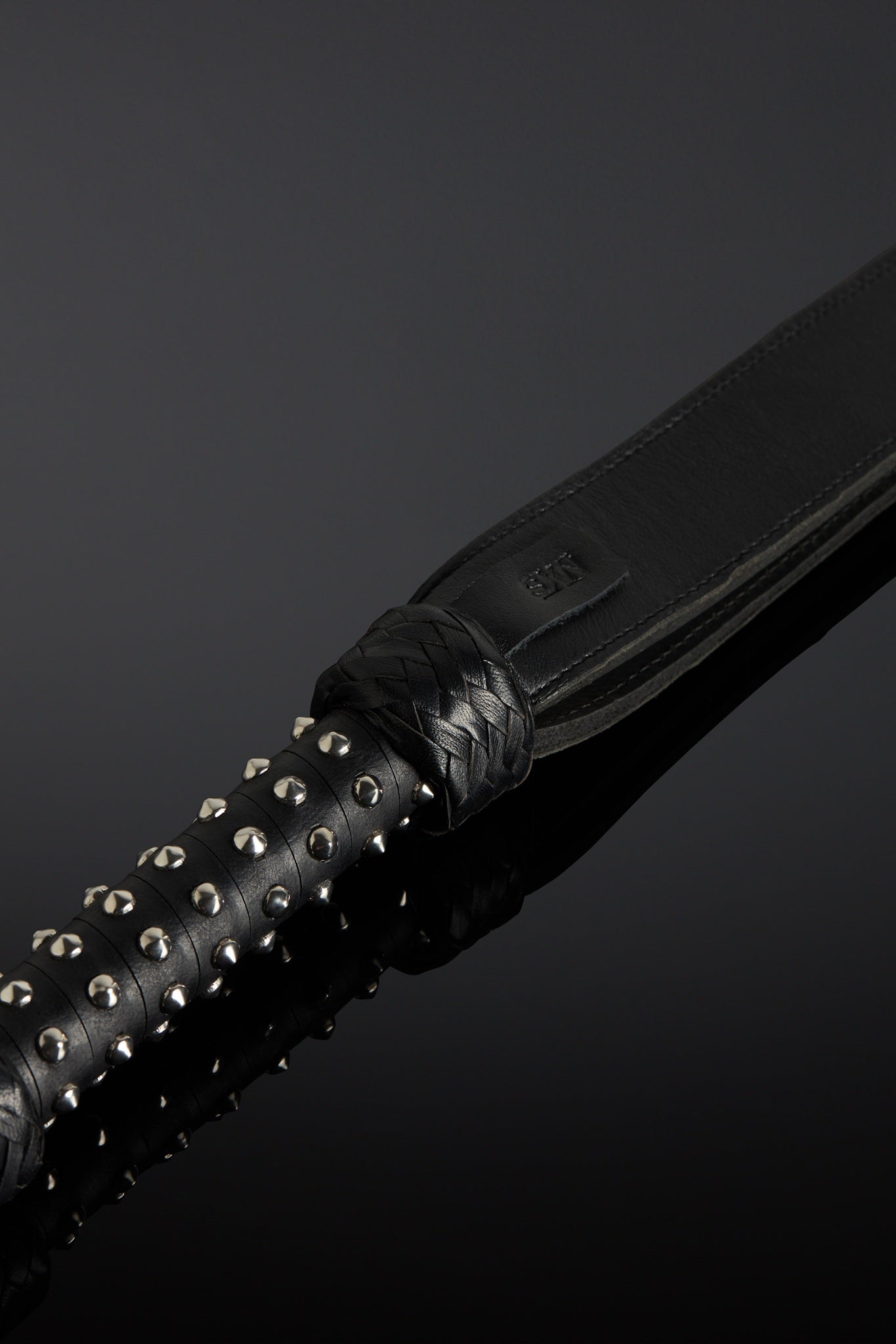 Black leather whip with a metal-adorned handle on a dark background