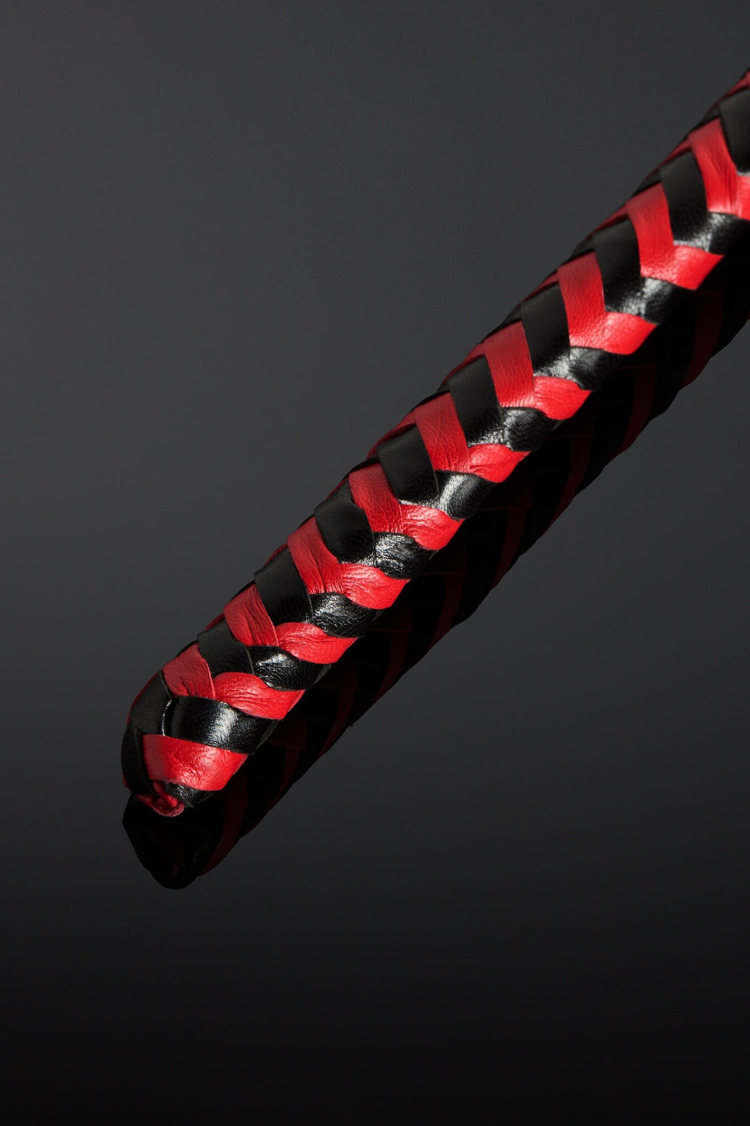 Black and red braided leather strap on a dark background. Close up shot of tip of whip