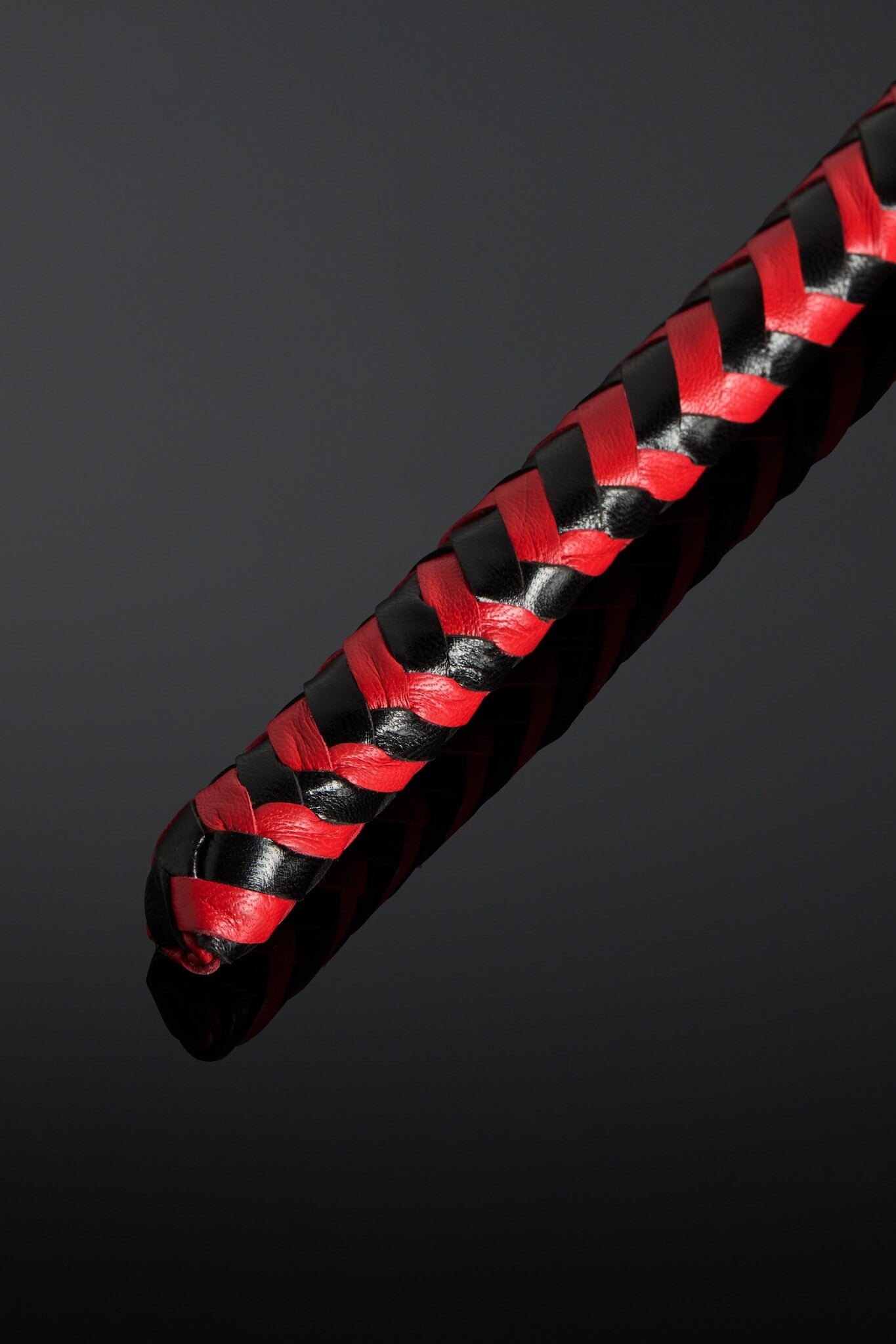 Black and red braided leather strap on a dark background. Close up shot of tip of whip