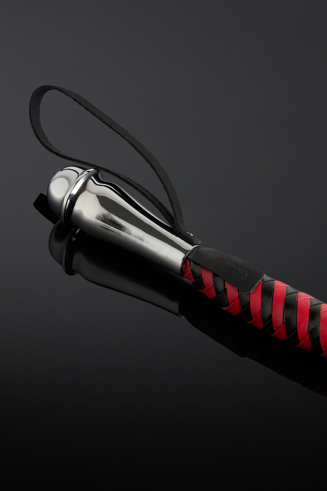 Close-up of a black and red leather tail with a metallic handle grip on a dark background