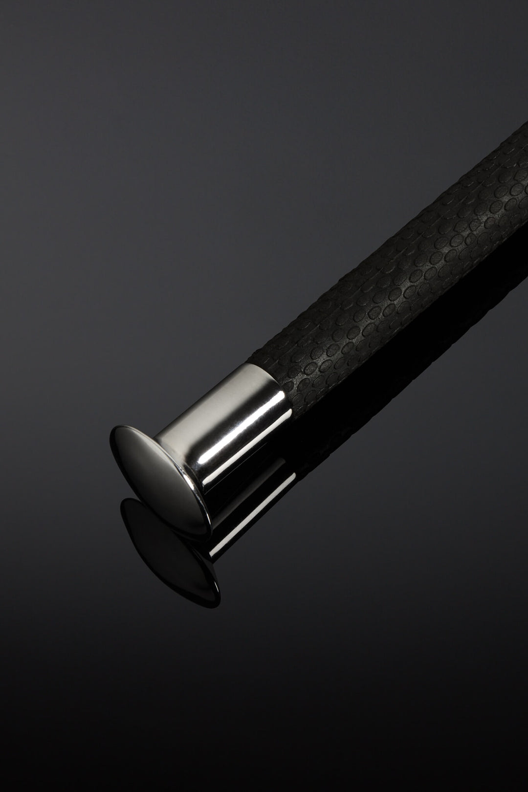 Close-up of a black textured cane handle with a silver ferrule on a dark background