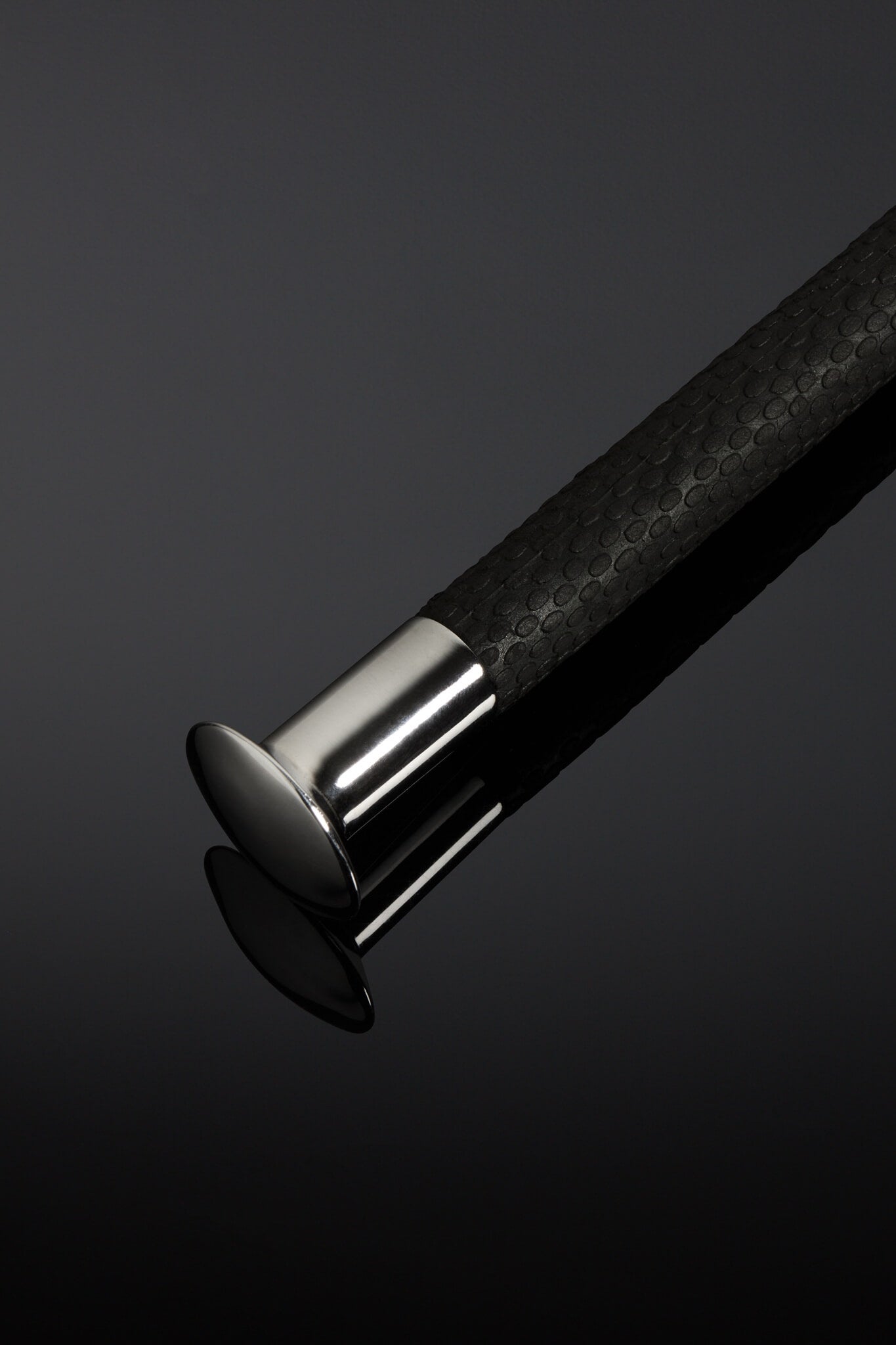 Close-up of a black textured cane handle with a silver ferrule on a dark background