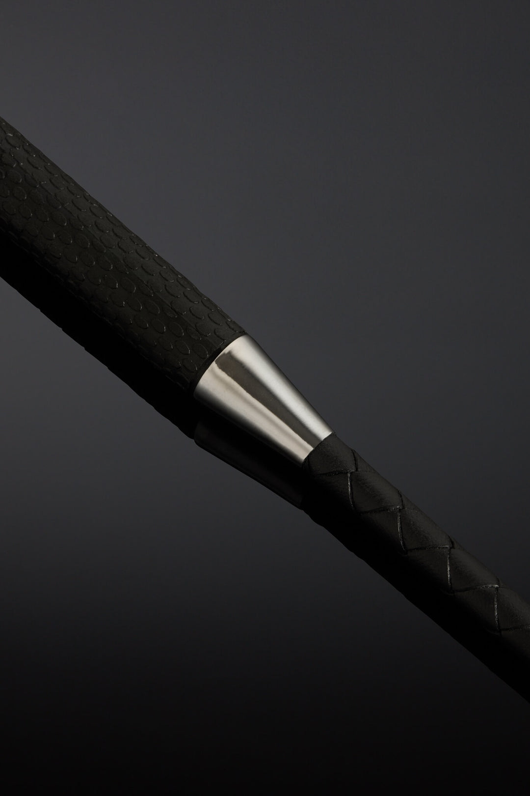 Close-up of a black braided cable with a silver metal accent on a dark background