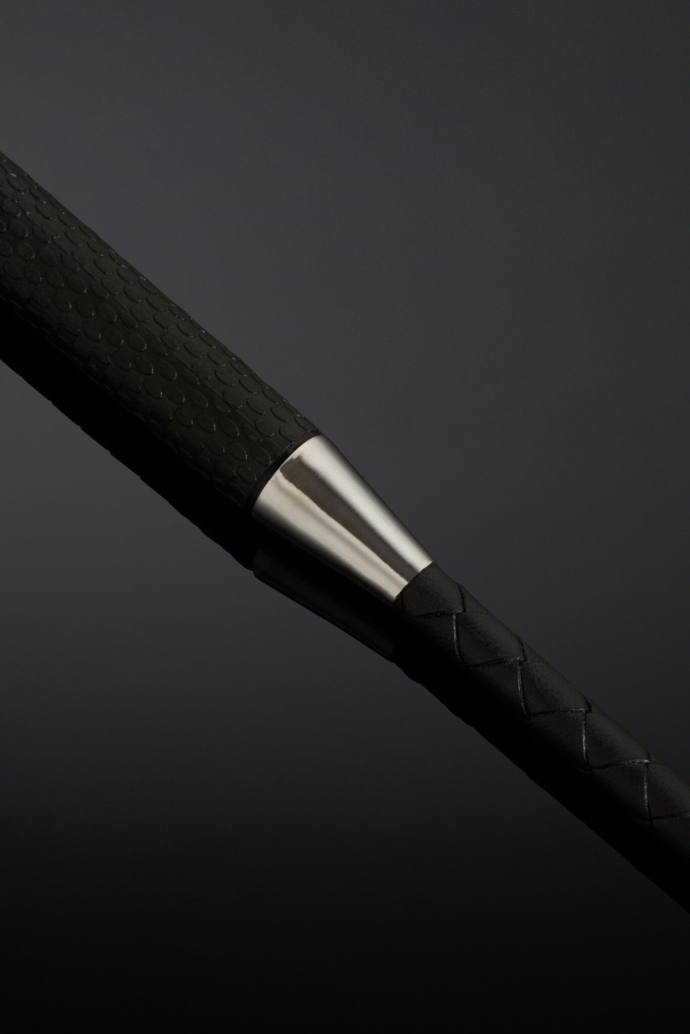 Close-up of a black braided cable with a silver metal accent on a dark background