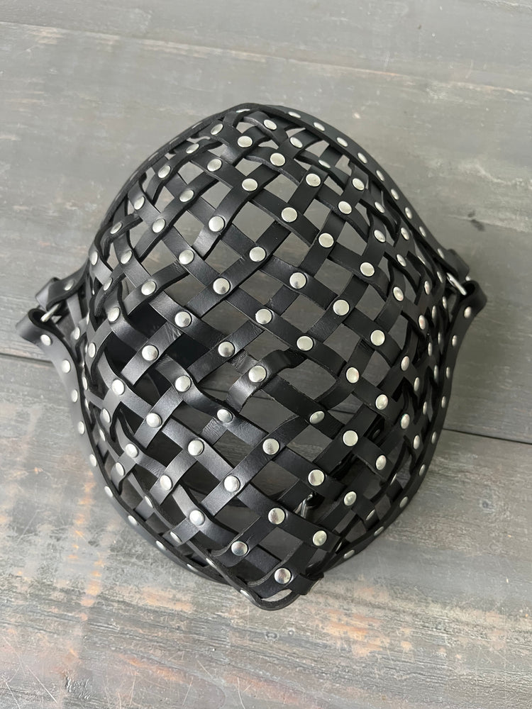 Photo showing a leather strapped mask with rivets laying on wooden table