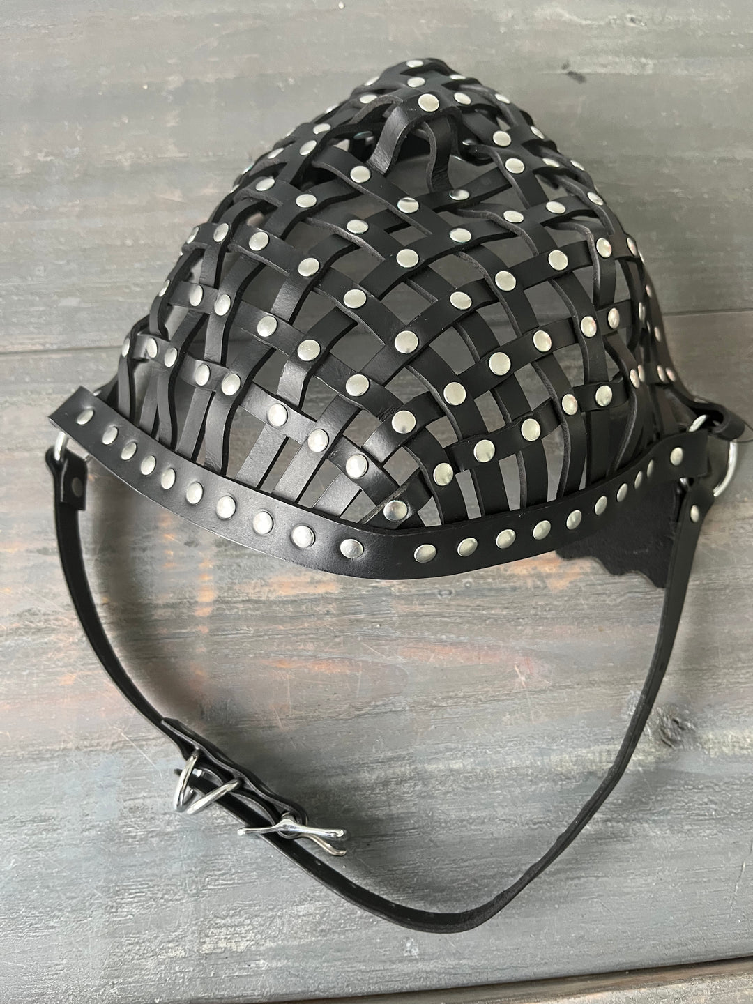 Photo showing a leather strapped mask with rivets laying on wooden table