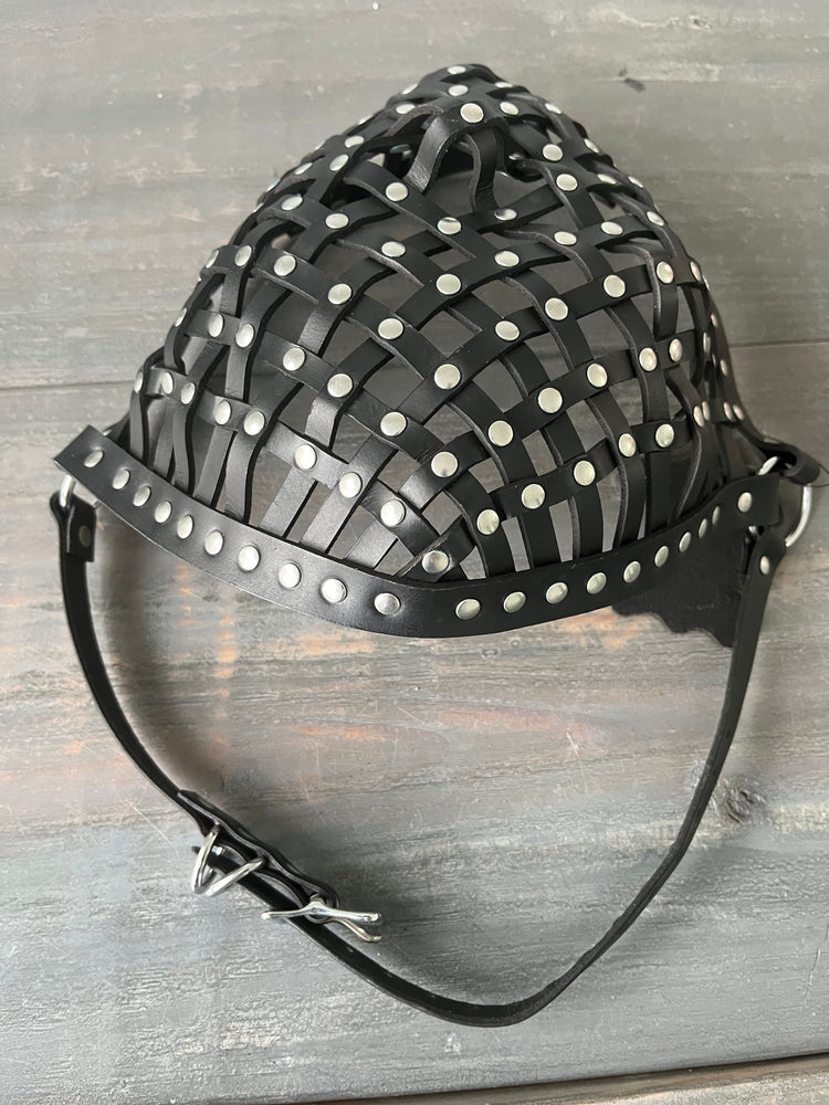Photo showing a leather strapped mask with rivets laying on wooden table