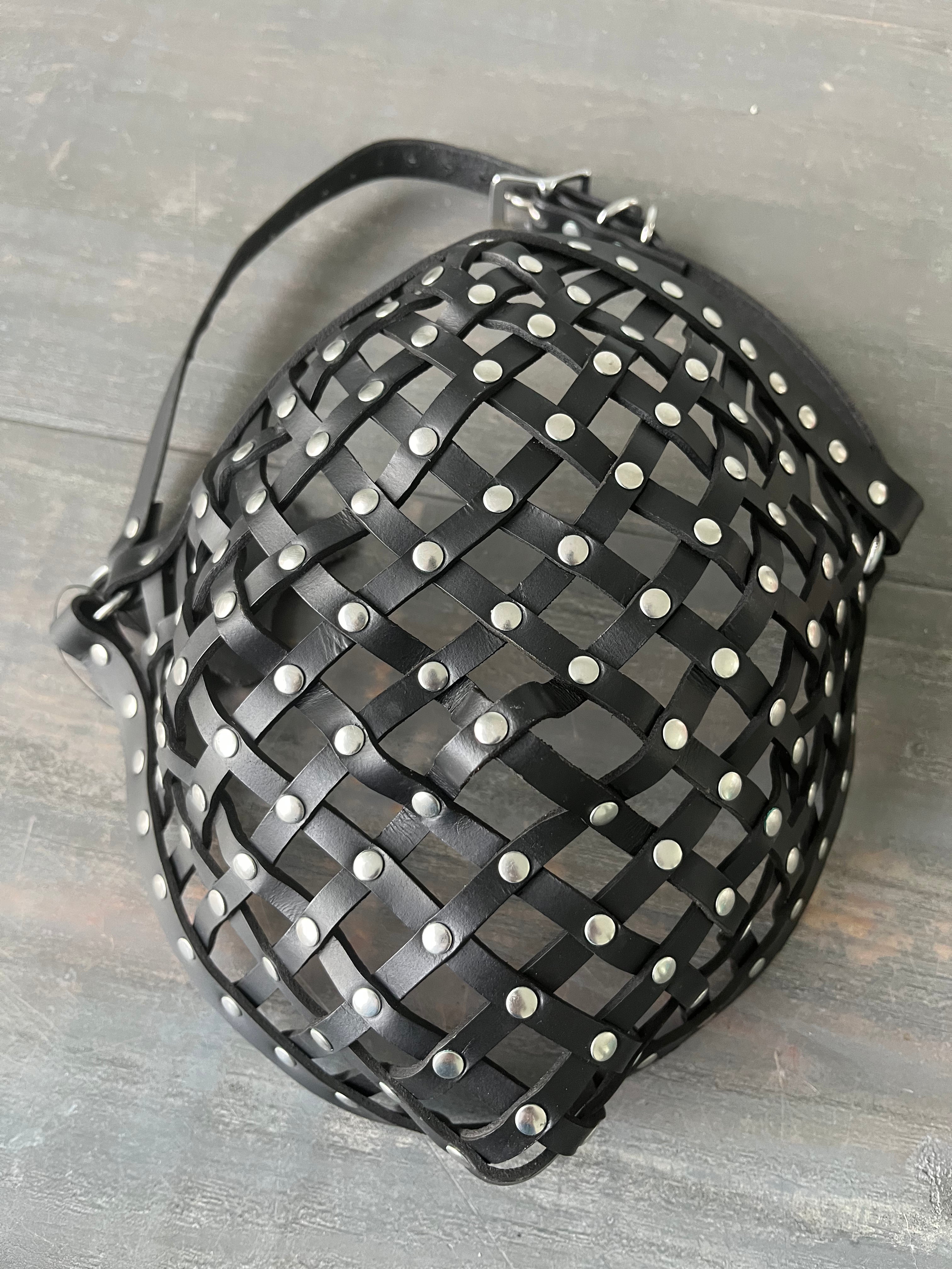 Photo showing a leather strapped mask with rivets laying on wooden table