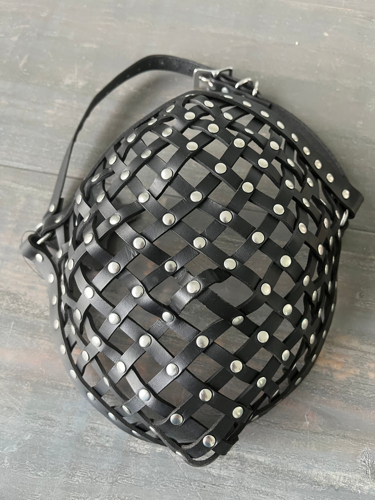 Photo showing a leather strapped mask with rivets laying on wooden table