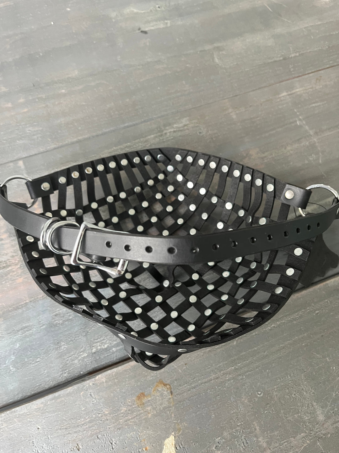 Photo showing a leather strapped mask with rivets laying on wooden table