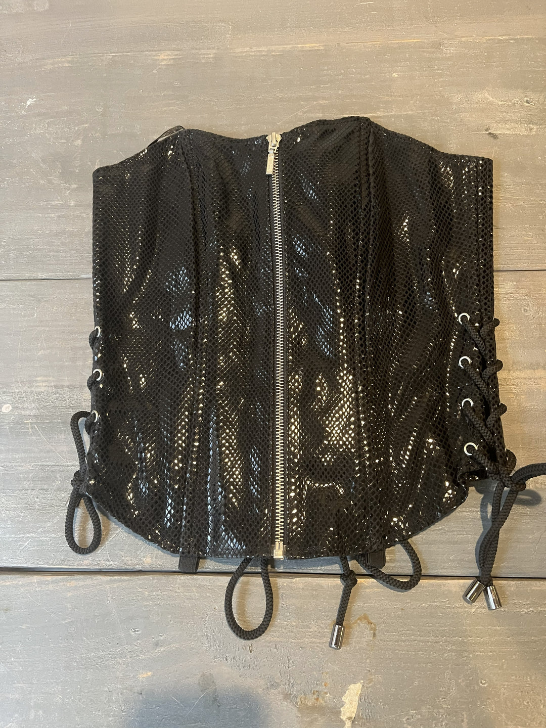Black leather corset lying on wooden table. 