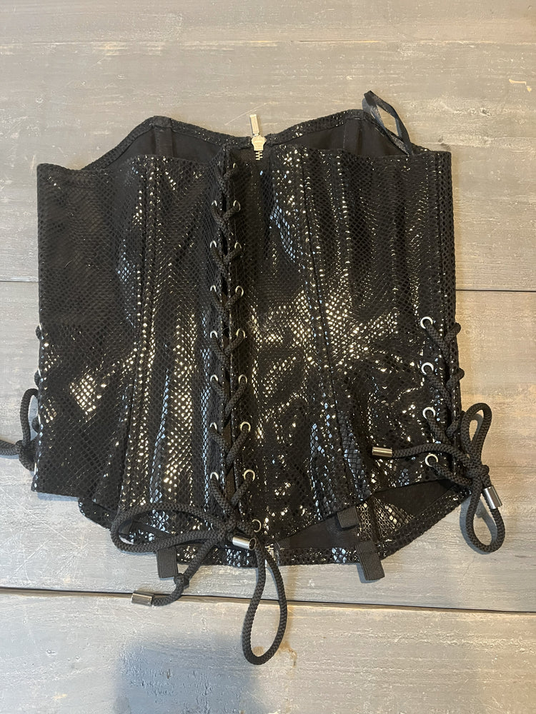 Black leather corset lying on wooden table. 