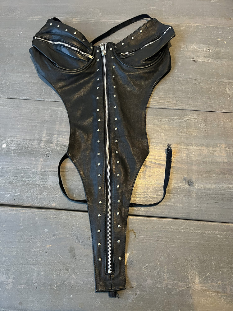 Black leather harness with studs and a zipper on a wooden surface