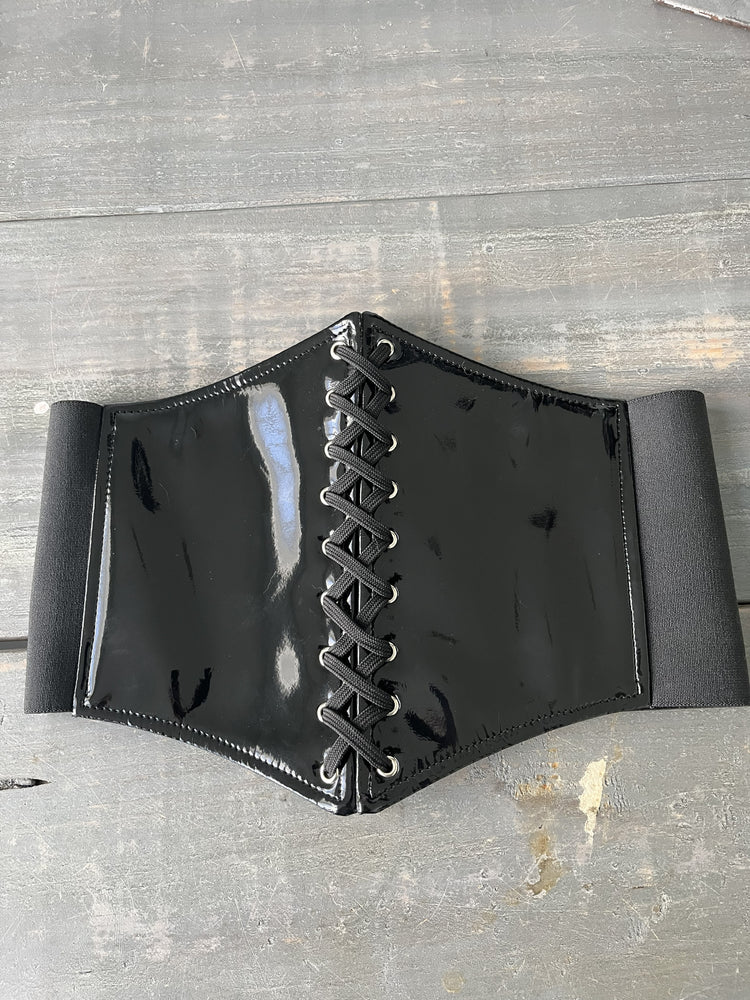Black leather corset belt with lace-up front on a gray wooden surface