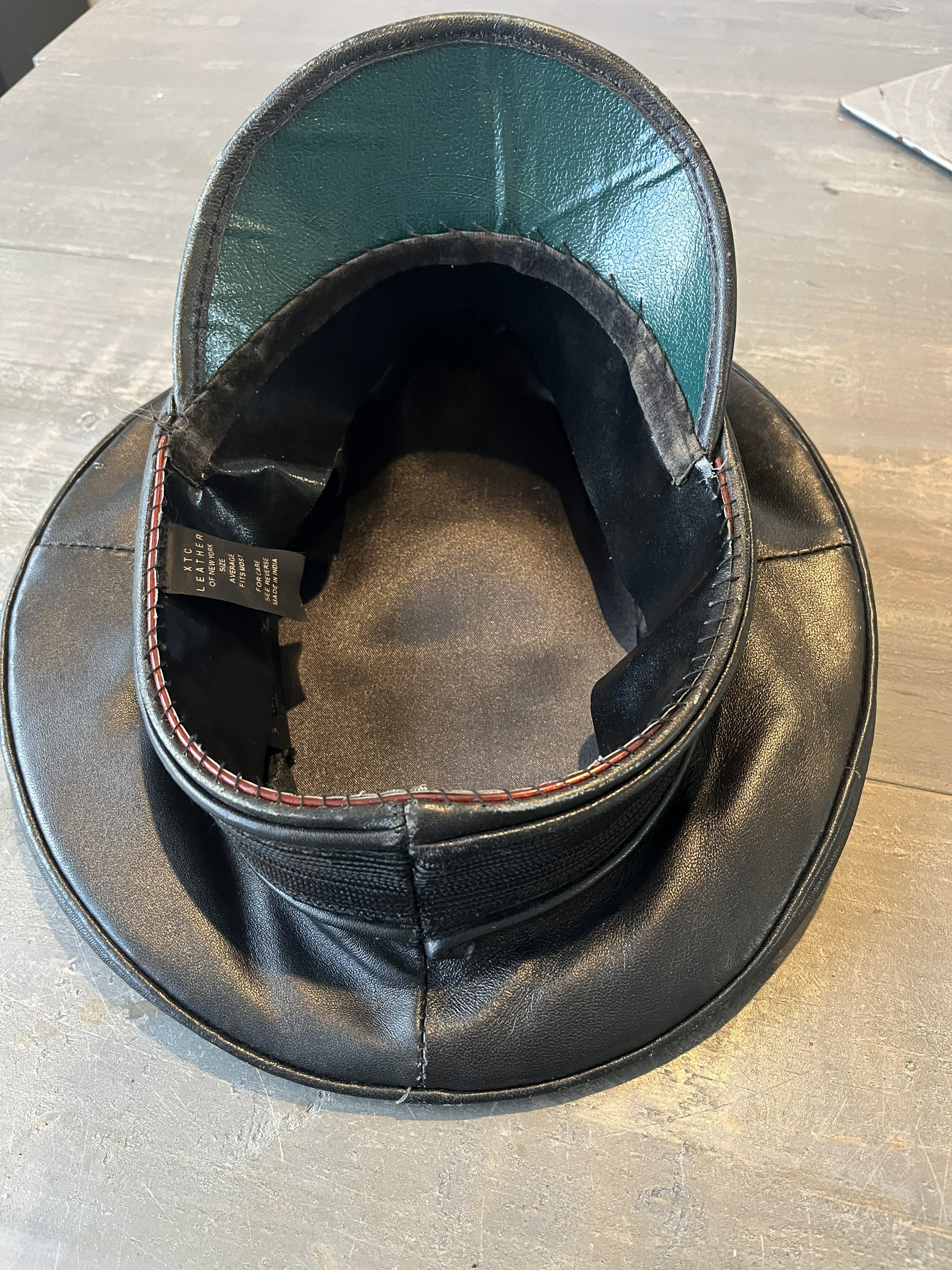 Black leather hat with a green interior on a wooden surface