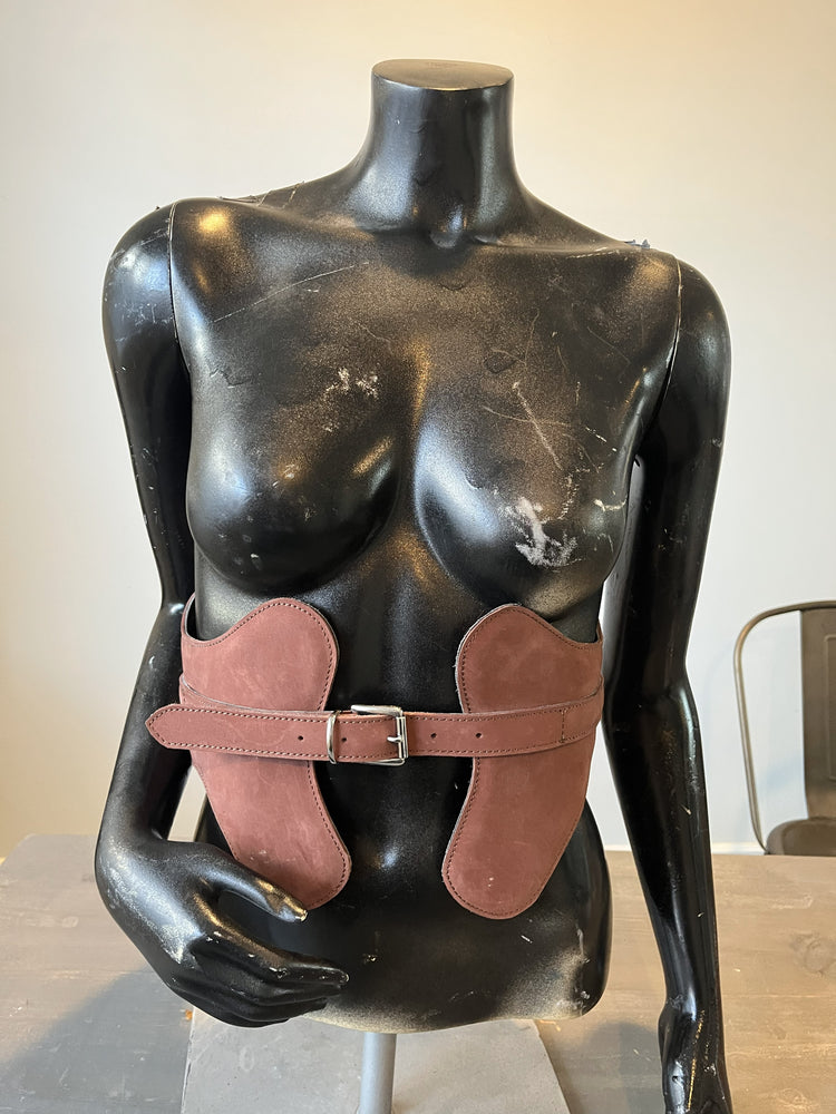 Mannequin torso with a brown leather harness on a neutral background