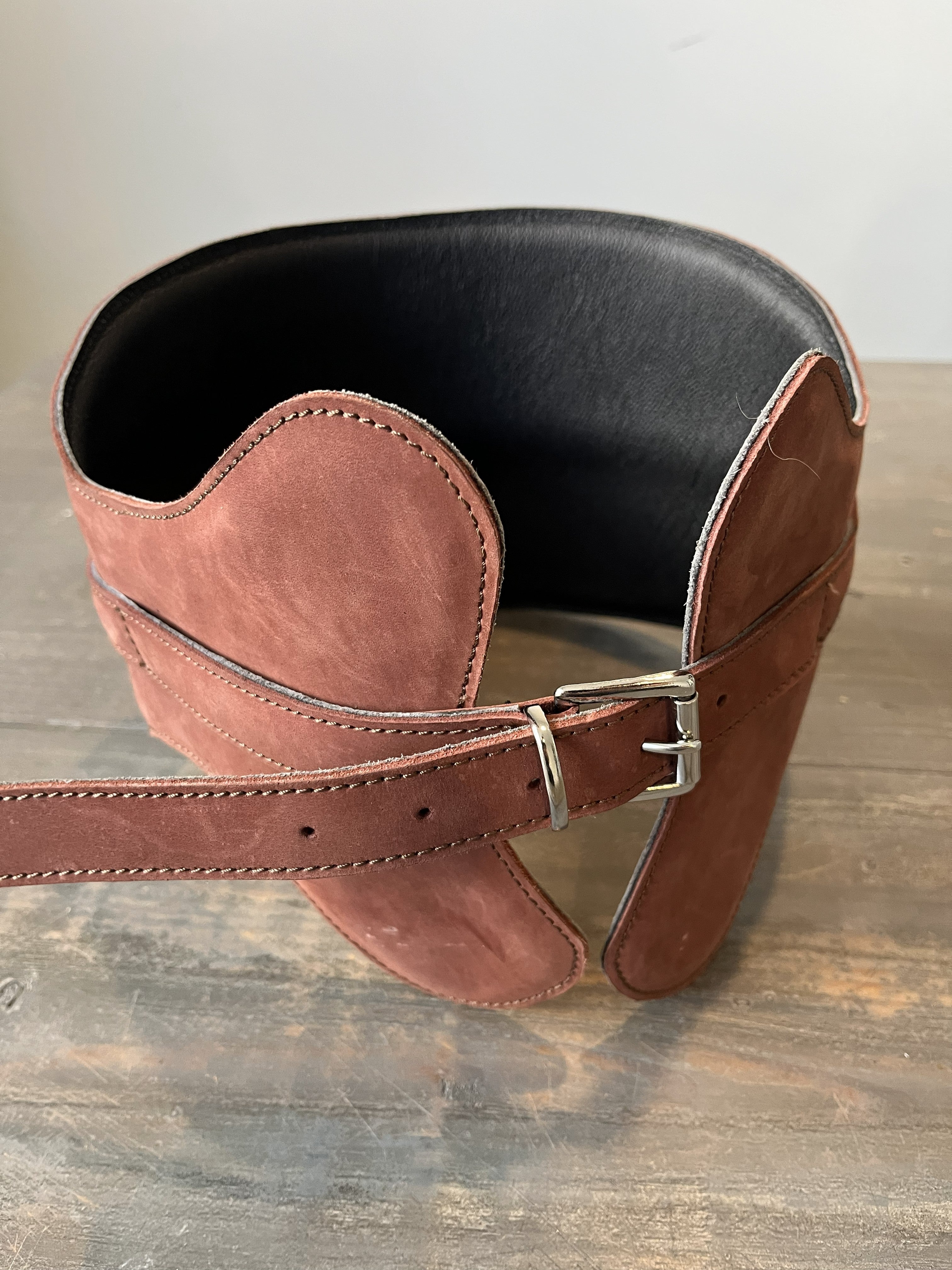 Brown leather girth strap with black leather padding on a wooden surface