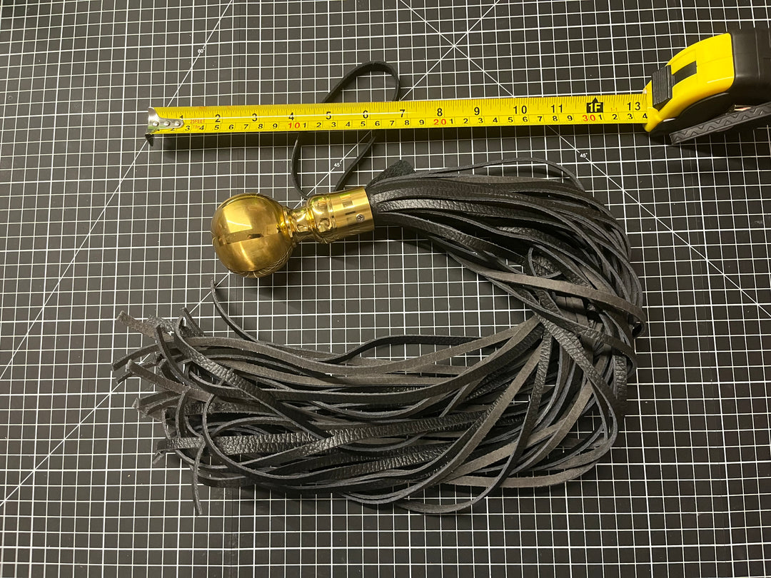 Black tassel with gold accent on a grid background, measured by a ruler.