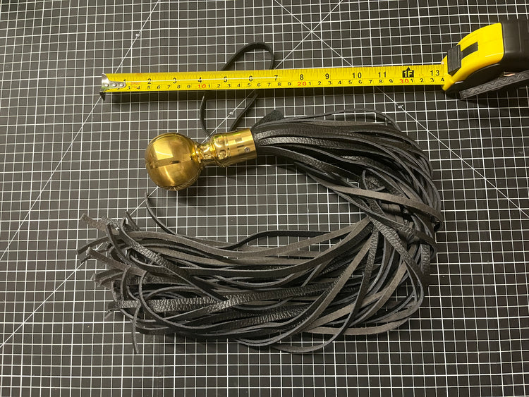 Black tassel with gold accent on a grid background, measured by a ruler.