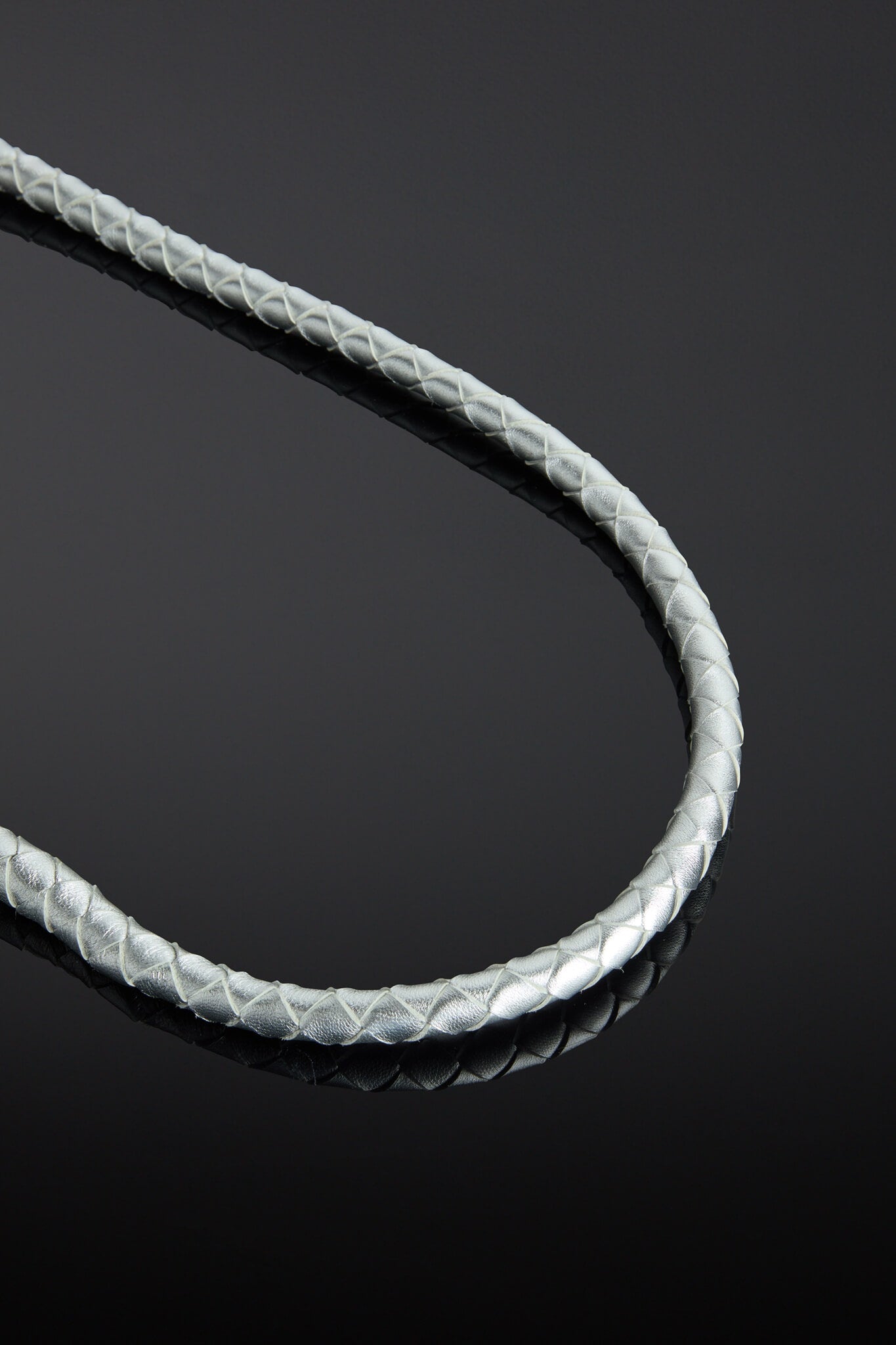 Close-up of a braided silver leather whip on a reflective black surface