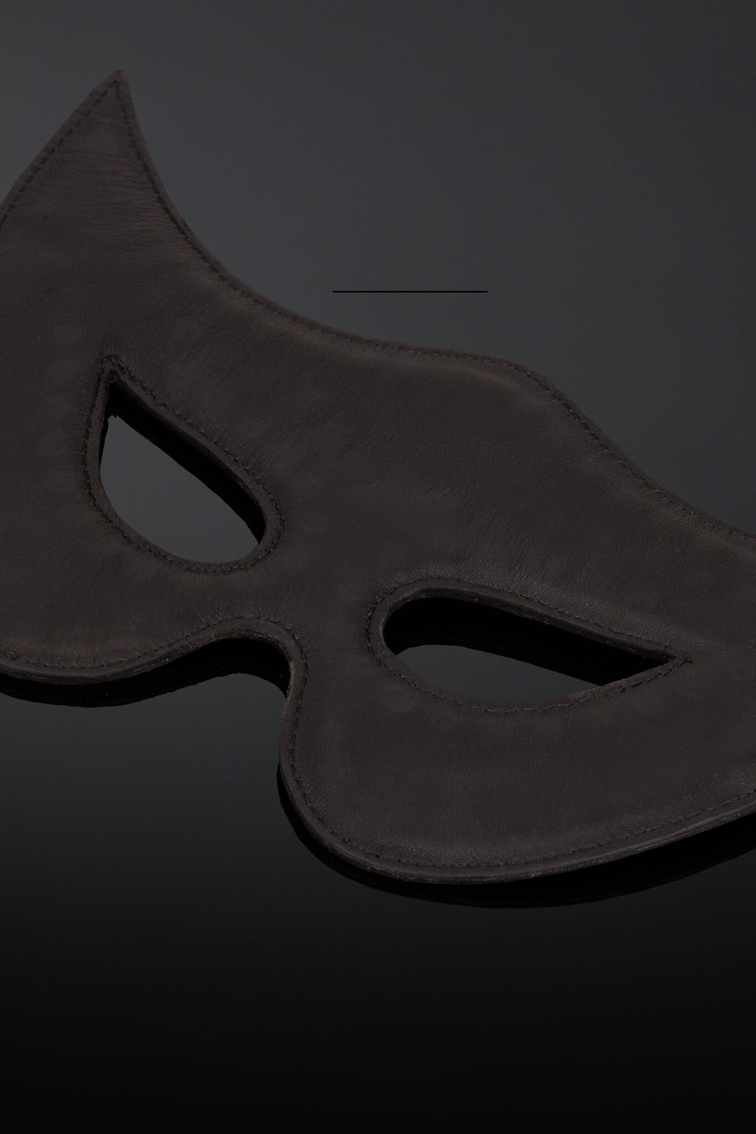 Interior shot of a black leather padded  masquerade mask with eye cutouts, shown on a dark reflective surface.