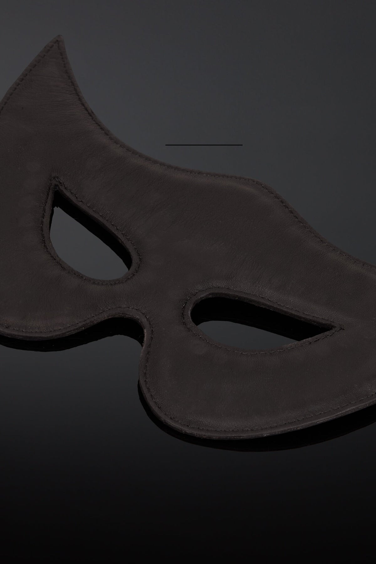 Interior shot of a black leather padded  masquerade mask with eye cutouts, shown on a dark reflective surface.