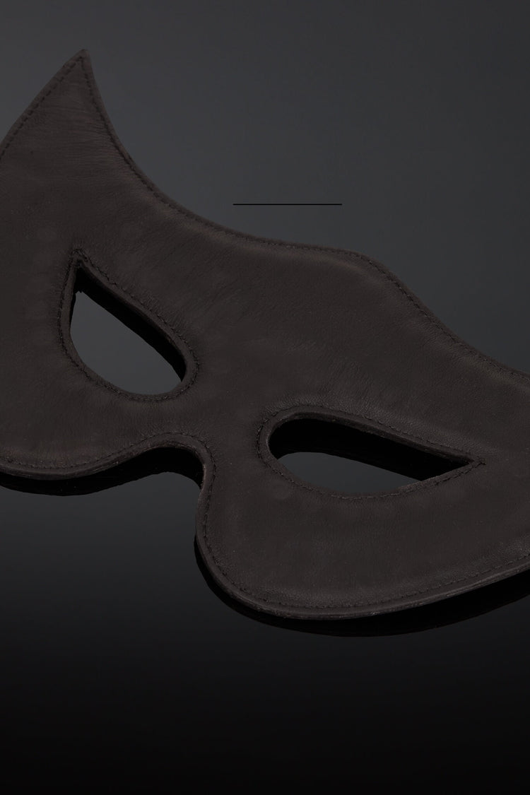 Interior shot of a black leather padded  masquerade mask with eye cutouts, shown on a dark reflective surface.
