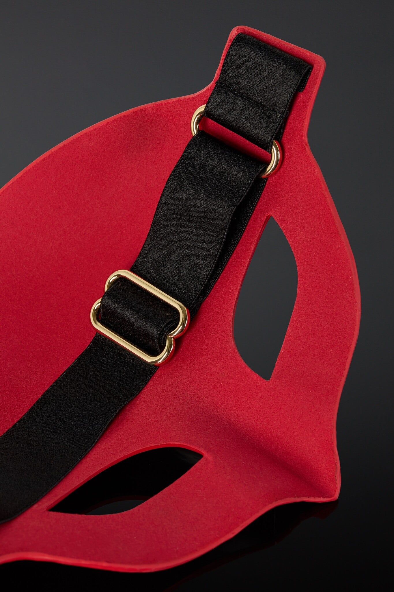 Red mask with black strap and gold buckle on a dark background