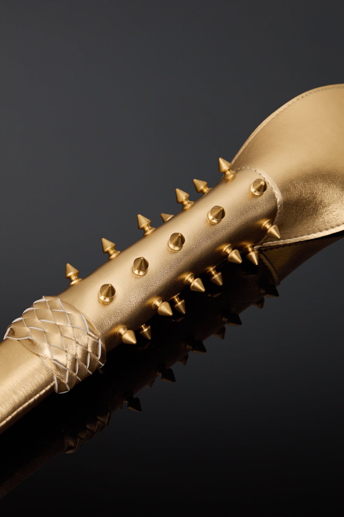 A close-up of a metallic gold leather handle featuring sharp gold-toned spikes along the side 