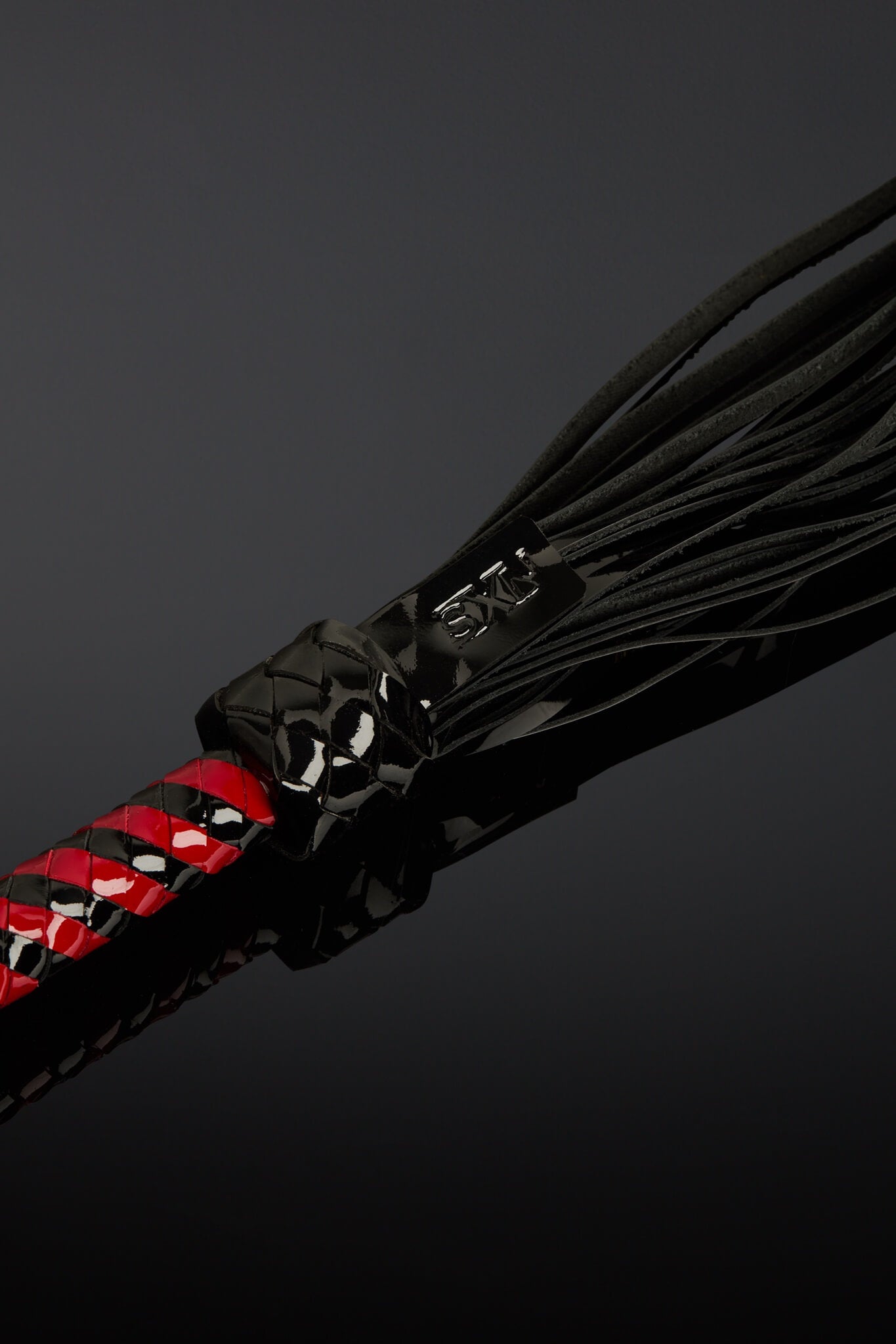 Black leather flogger with red accents on a dark background
