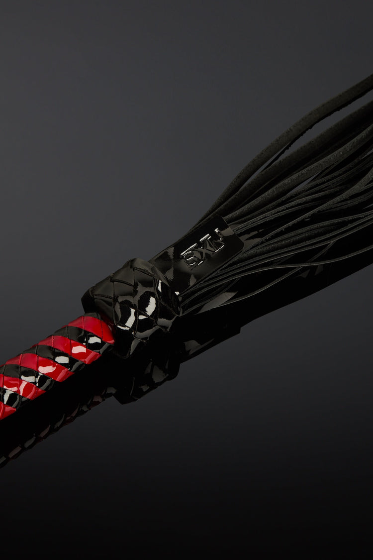 Black leather flogger with red accents on a dark background