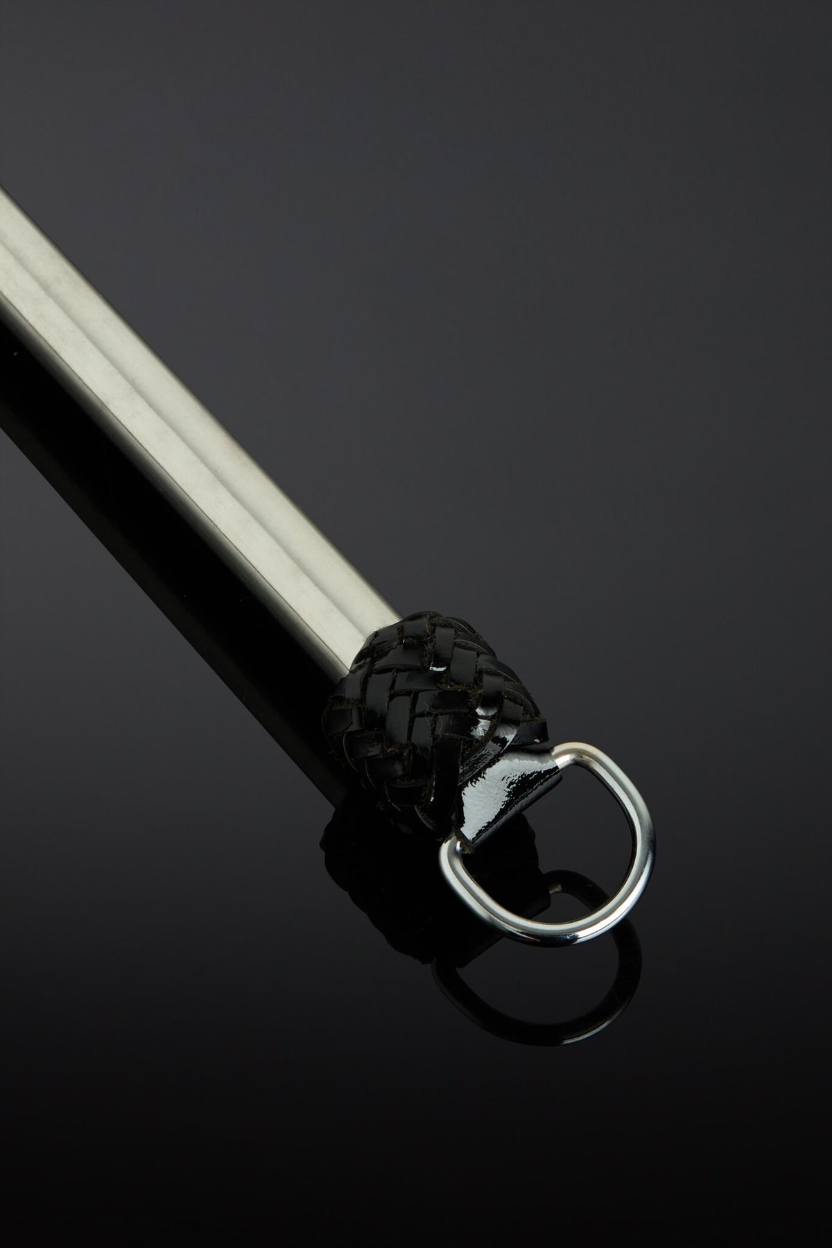 A close-up of a black leather-wrapped martial arts stick with a silver metal D-ring, set against a dark reflective background.