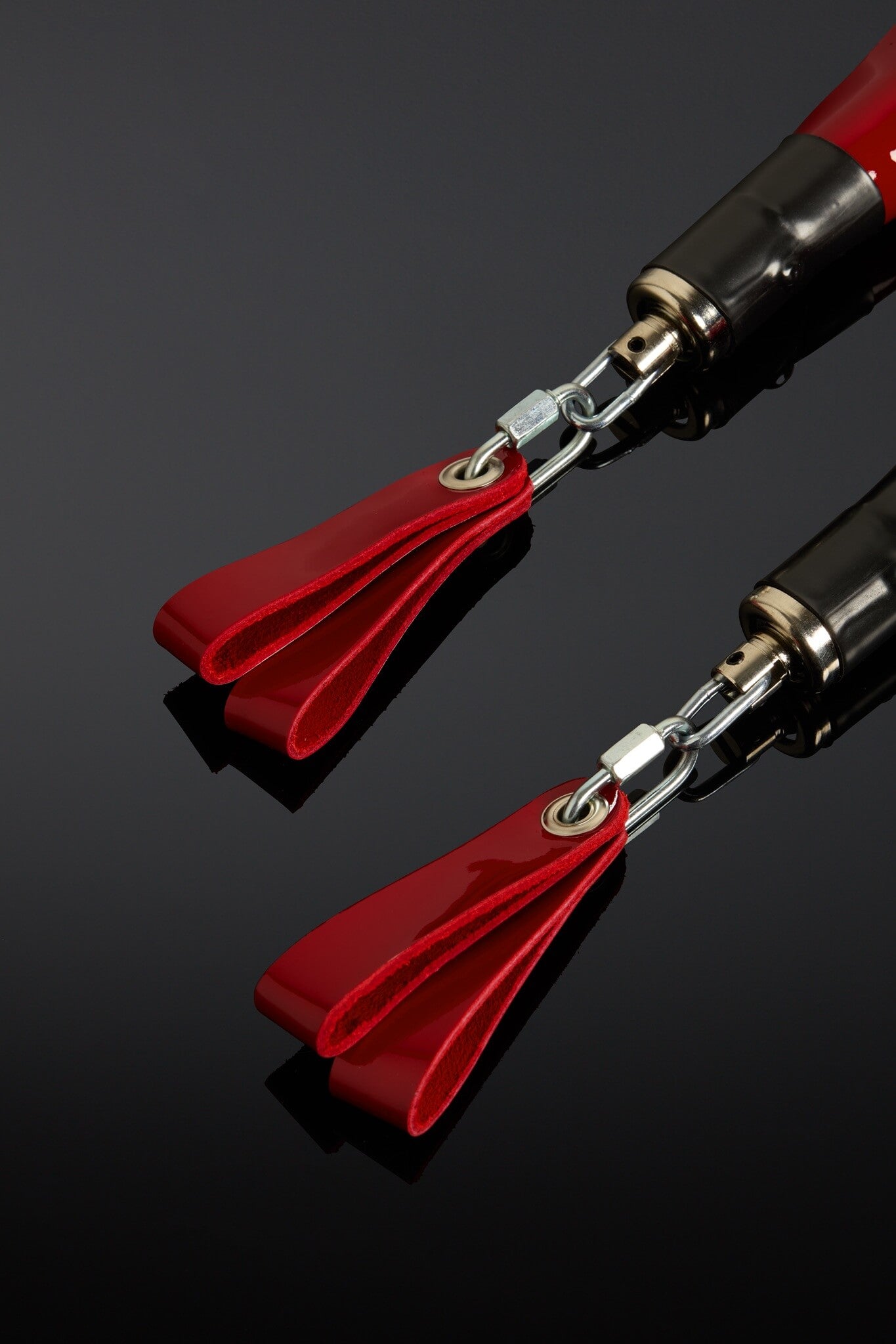 Two red and silver objects with tassels on a reflective black surface