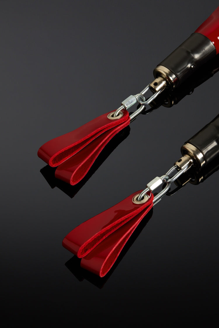 Two red and silver objects with tassels on a reflective black surface