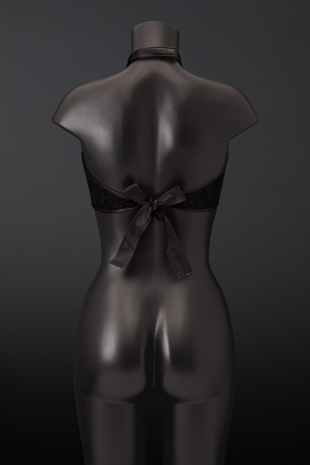 Black lace halter bra with a large leather back bow, displayed on a dark gray mannequin from the back against a dark gray background.