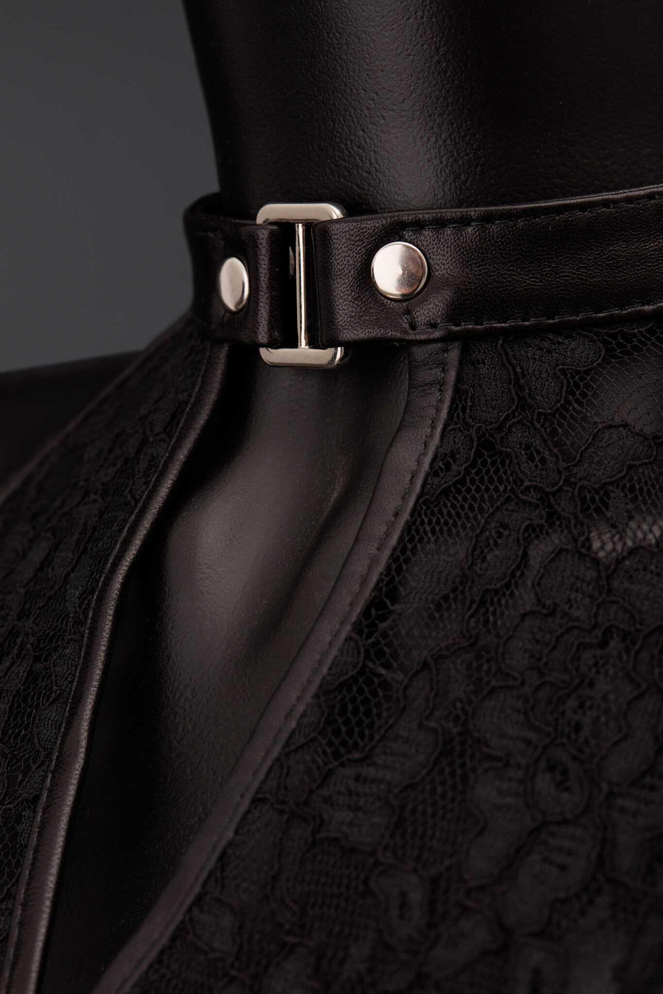 Close-up of a black eather collar with a silver metal buckle and silver rivets, worn on a black mannequin torso. The collar is paired with a black lace garment.