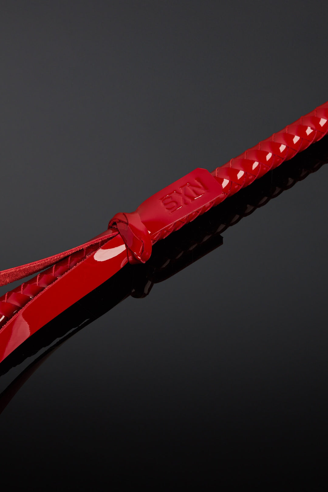 Red tag with SXN logo on the base of a crop handle. Laying on black background