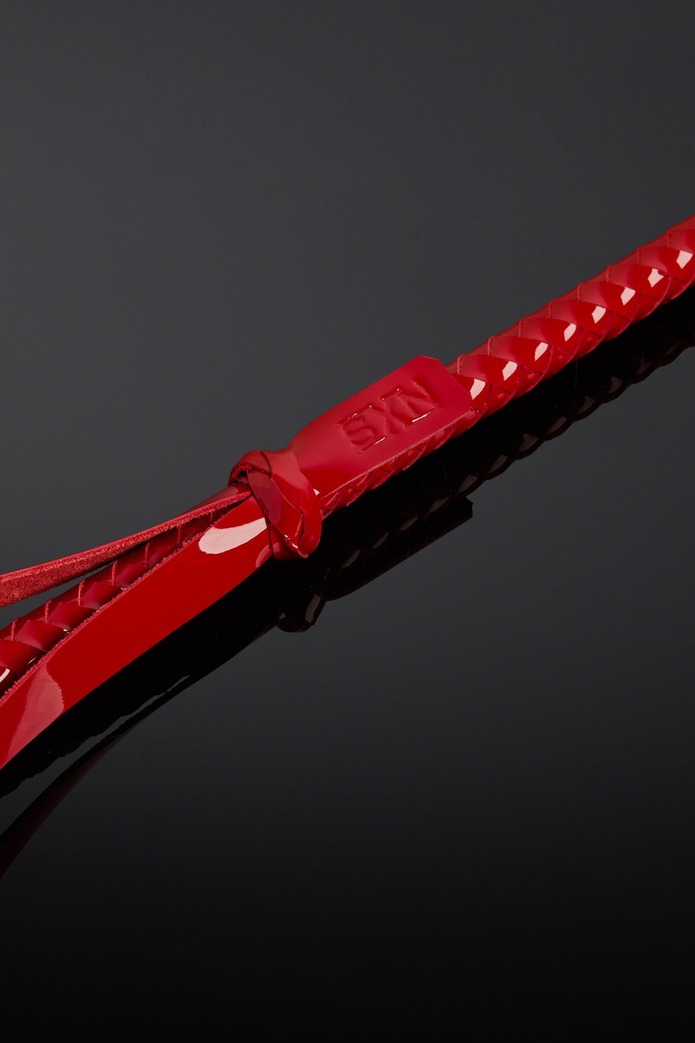 Red tag with SXN logo on the base of a crop handle. Laying on black background