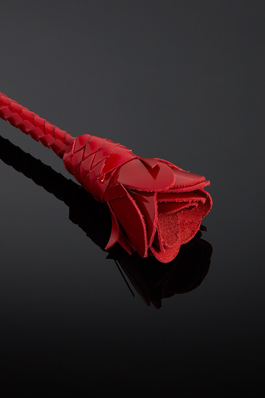 Red rose-shaped object on a reflective black surface with a dark background
