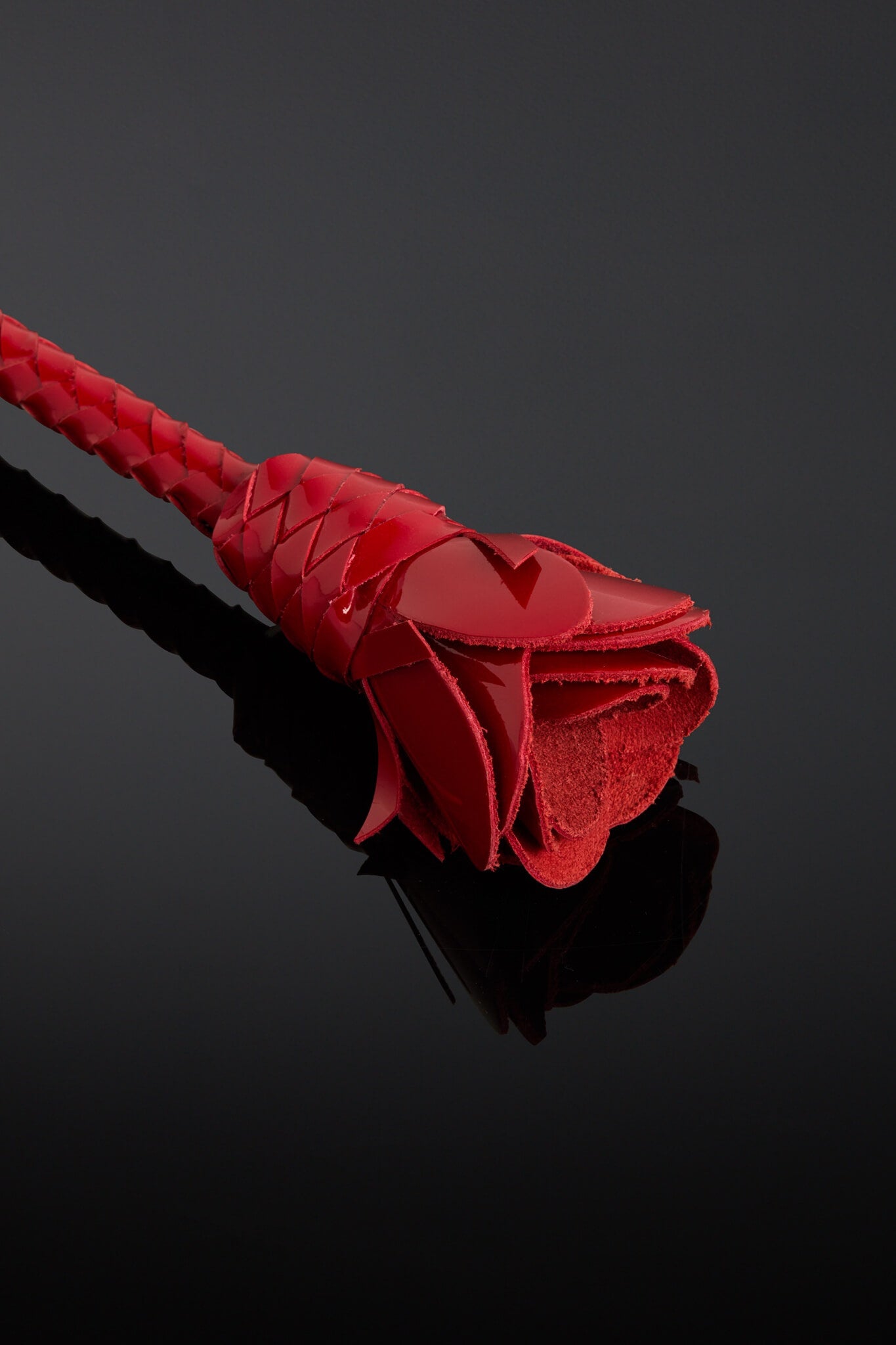 Red rose-shaped object on a reflective black surface with a dark background