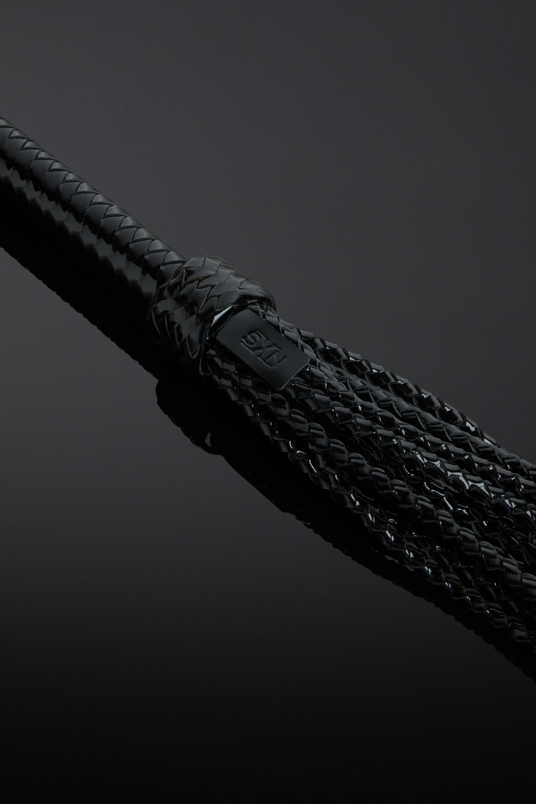 Close-up of a braided black flogger tails on a dark background 