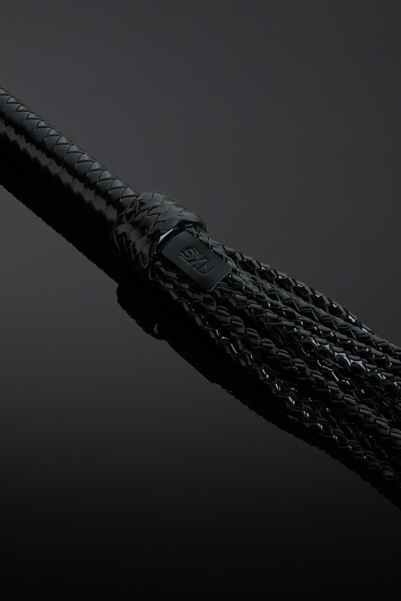 Close-up of a braided black flogger tails on a dark background 