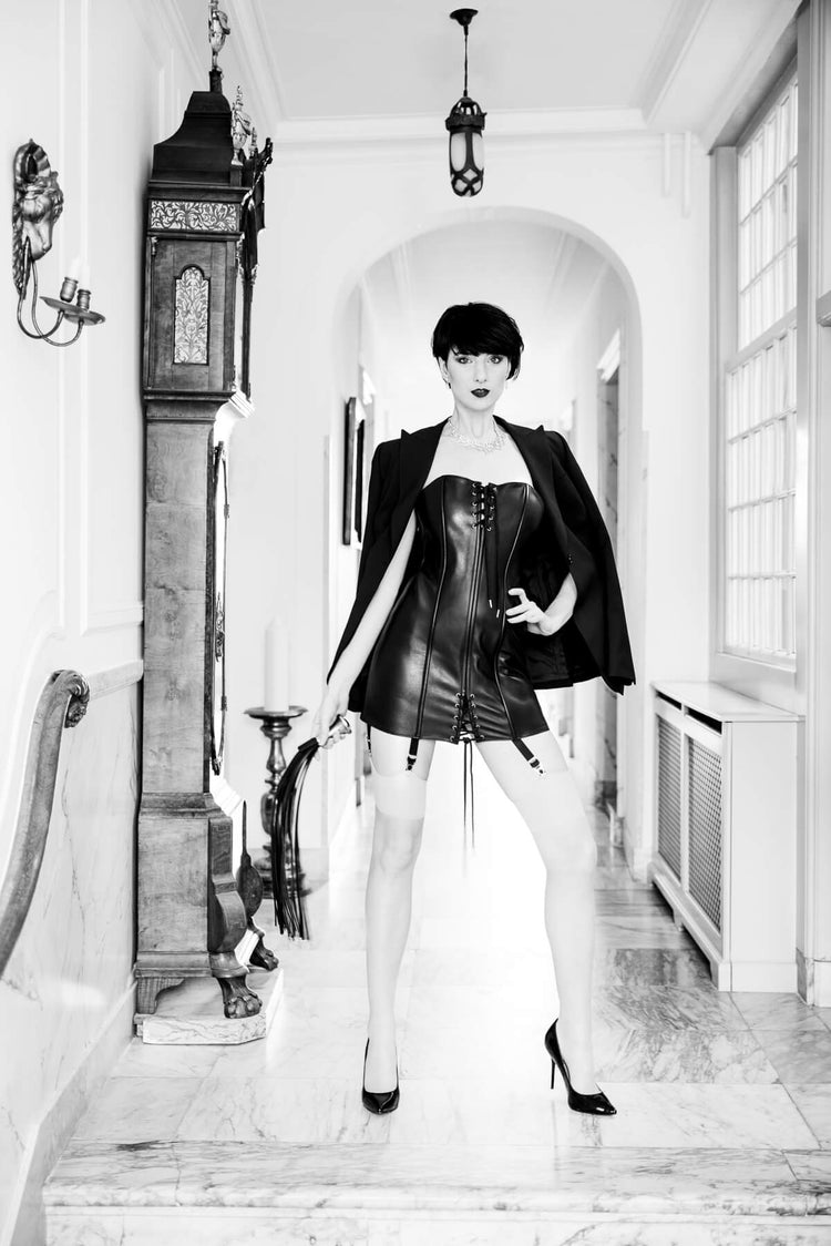 Person in a stylish outfit standing in an elegant hallway with a grandfather clock.
