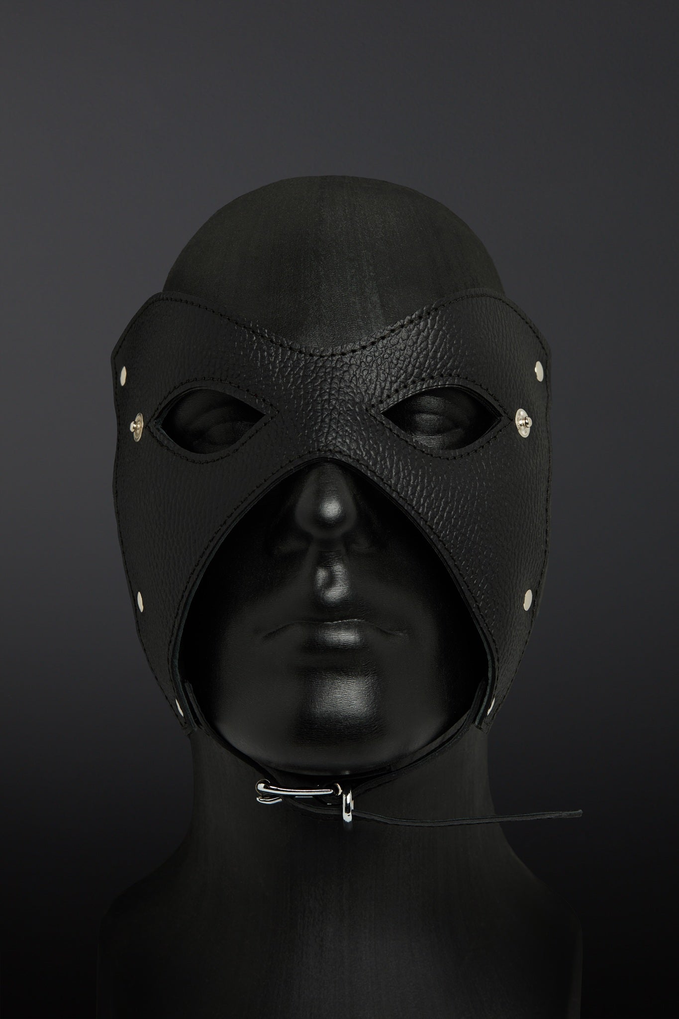 Black leather hood with eye and nose holes on a dark background